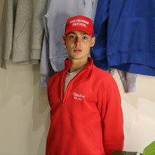 Load image into Gallery viewer, Male model in red 1/4 zip sweatshirt with embroidered logo, wearing red cap, surrounded by hoodies in various colors.