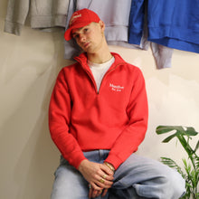 Load image into Gallery viewer, Unisex red cotton 1/4 zip sweatshirt with embroidered logo, styled with casual jeans and a red cap.