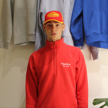 Load image into Gallery viewer, Unisex red cotton 1/4 zip sweatshirt with Manifest logo, displayed with various hoodies in background.