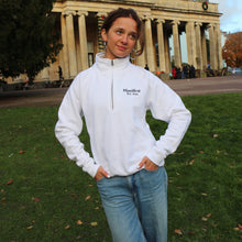 Load image into Gallery viewer, Female model wearing a white 1/4 zip sweatshirt with Manifest logo, posing outdoors in a park setting.