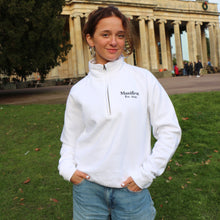 Load image into Gallery viewer, Female model wearing a white Manifest unisex 1/4 zip sweatshirt in a park setting.