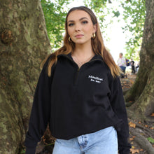 Load image into Gallery viewer, Female model wearing a Manifest black 1/4 zip sweatshirt outdoors, showcasing the embroidered logo.