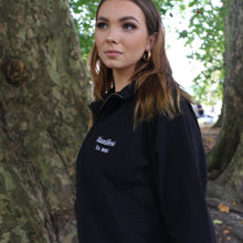 Load image into Gallery viewer, Female model wearing a stylish Manifest black 1/4 zip sweatshirt standing against a tree backdrop.