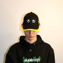 Load image into Gallery viewer, Manifest black and yellow cap with detailed anime eye embroidery, adding a unique and playful touch to your outfit.

