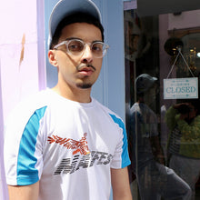 Load image into Gallery viewer, Man wearing a white and blue Manifest Clothing t-shirt , standing in front of a store entrance.
