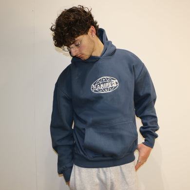 Person wearing a blue hoodie with a logo and gray pants against a plain background