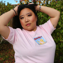 Load image into Gallery viewer, Person wearing a pink t-shirt with a cartoon cat and text, standing outdoors with greenery in the background.

